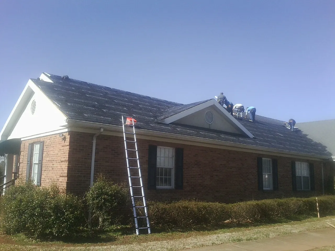 Crew tearing shingles off a brick ranch roof with a ladder set — Metal Roof Repair work by our crew in Courtland