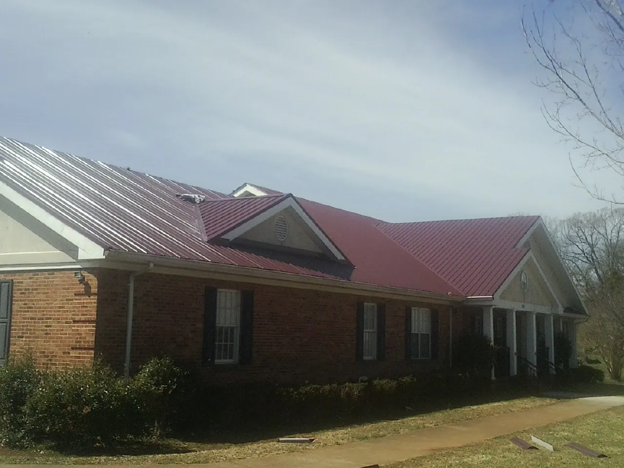 Red metal roof with gabled entries on a long brick building, from a Hail Damage Roof Repair job in Courtland