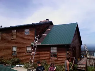 Green metal roof going on a two story log home with ladders set in Courtland
